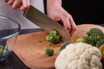 young woman in a gray aprons cuts cauliflower broccoli
