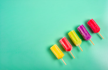 multi-color popsicles line up on green background with copy space
