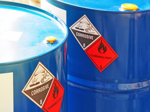 the close-up shot of blue color hazardous dangerous chemical barrels ,have warning labels of corrosive & flammable liquid in daylight on daytime.