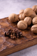 Bunch of walnuts on carved wooden board, bright background. Healthy nuts and seeds composition, background.