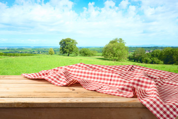 Empty wooden table with tablecloth over summer meadow background