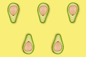 Rows of five scattered tasty fresh halves of organic avocado with kernels in center of yellow table in kitchen or market. Top view. Cooking concept