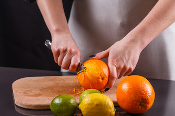 young woman in a gray aprons, cuts an orange zest