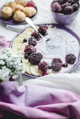 fruity yogurt with banana slices, frozen forest fruits and almond nut flakes on a plate surrounded by frozen berries and sweet buns