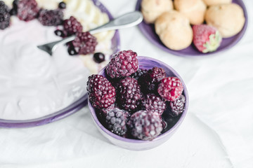 fruity yogurt with banana slices, frozen forest fruits and almond nut flakes on a plate surrounded by frozen berries and sweet buns