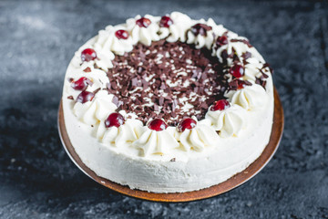 German, delicious Black Forest cake, with a delicate white cream, cherries in alcohol and dark chocolate on a dark stone table 