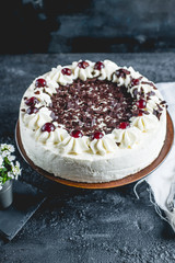 German, delicious Black Forest cake, with a delicate white cream, cherries in alcohol and dark chocolate on a dark stone table decorated with white linen fabric