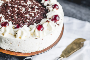 German, delicious Black Forest cake, with a delicate white cream, cherries in alcohol and dark chocolate on a dark stone table decorated with white linen fabric