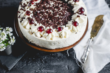 German, delicious Black Forest cake, with a delicate white cream, cherries in alcohol and dark chocolate on a dark stone table decorated with white linen fabric