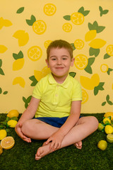 The boy sits and eats lemons and limes, smiles and twists from citrus acid