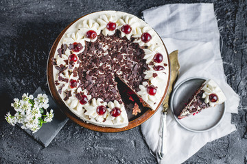 German, delicious Black Forest cake, with a delicate white cream, cherries in alcohol and dark chocolate on a dark stone table decorated with white linen fabric