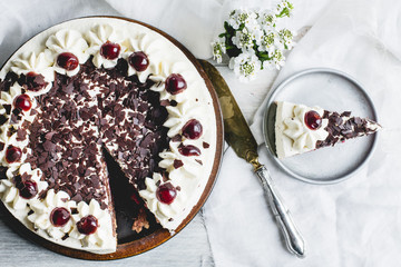 German, delicious Black Forest cake, with a delicate white cream, cherries in alcohol and dark chocolate on a white wooden background decorated with white linen fabric and white flowers