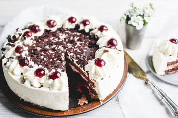 German, delicious Black Forest cake, with a delicate white cream, cherries in alcohol and dark chocolate on a white wooden background decorated with white linen fabric and white flowers