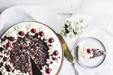 German, delicious Black Forest cake, with a delicate white cream, cherries in alcohol and dark chocolate on a white wooden background decorated with white linen fabric and white flowers