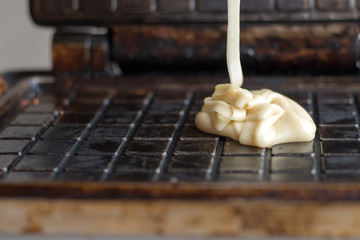 White batter into the waffle iron baking waffles Waffle batter on the hot surface of waffle maker for baking delicious crispy wafers for dessert or Breakfast 