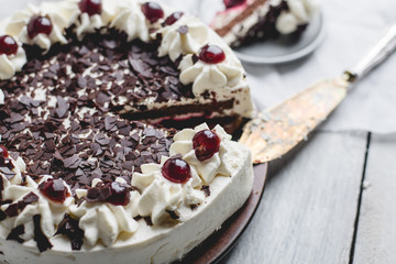 German, delicious Black Forest cake, with a delicate white cream, cherries in alcohol and dark chocolate on a white wooden background decorated with white linen fabric