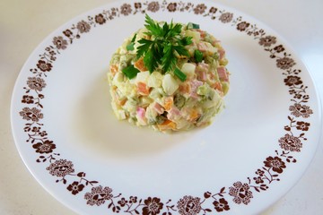 salad of boiled vegetables, eggs, ham and parsley on a white plate close-up