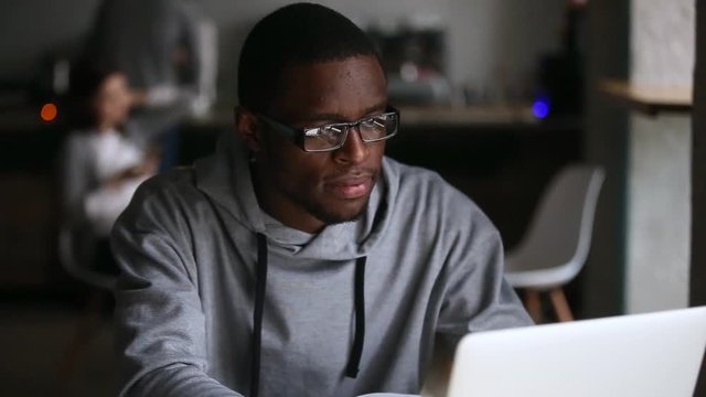 Millennial african student studying with book using laptop in cafe