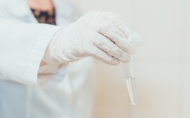 A doctor in white gloves holding a test tube with sample with a hand in the medical laboratory closeup. Concept of medicine and science