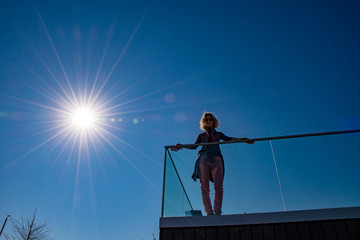 young woman standing on the top of a house with blue sky and sun