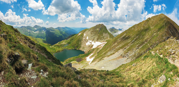 panorama of fagaras mountain in summer. glacier lake capra between hills. beautiful landscape with steep slopes, grassy meadows and peak. wonderful weather with gorgeous cloudscape on the blue sky