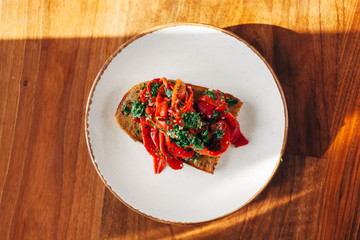 Roasted red peppers on a toasted bread with parsley and olive oil served on a plate