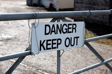 Danger keep out sign on metal gate boundary to disused contaminated factory site