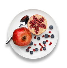 blueberries and pomegranate with a silver spoon on white plate
