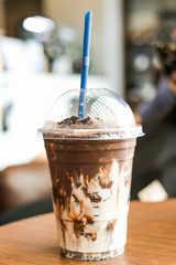 Iced rich chocolate in take a way cup on wooden table at coffee shop.