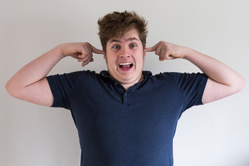 Teenage boy in dark blue shirt putting a finger in his ears to demonstrate loud noise and making a funny open-mouthed face