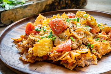 farfalle pasta in tomato sauce with chicken and pork on wooden plate