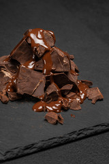 dark or milk chocolate pieces stack and chocolate syrup on dark concrete background