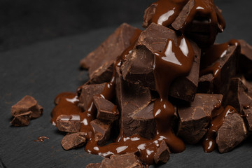 dark or milk chocolate pieces stack and chocolate syrup on dark concrete background