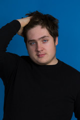 Vertical photo of round faced blue eyed teenager boy in dark sweater combing his thick brown hair with his right hand