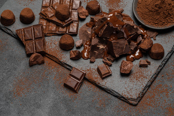 dark or milk chocolate pieces, chocolate syrup and truffle candies on dark concrete background
