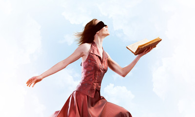 Girl against cloudy sky with opened book in palm as idea for knowledge