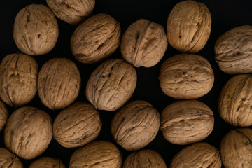 Walnuts in the shell lying on black surface, top view. Background of round walnuts. Healthy nuts and seeds background.