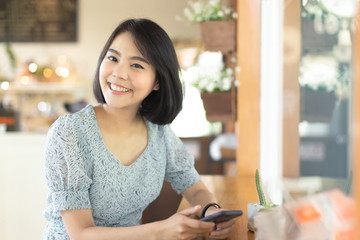young asian woman smiling and holding smartphone in hands with copy space