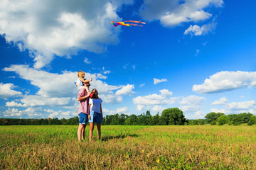 Mother, father and daughter are flying a kite in the field. Front view, copy space.