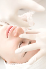 Naklejka premium a girl in a white sterile hat is lying on a couch by a beautician and she is given injections to smooth out wrinkles around the eyes