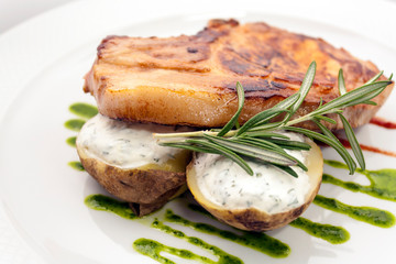 juicy piece of pork chop with potatoes stuffed with creamy sauce, rosemary and kiwi sauce on a white plate