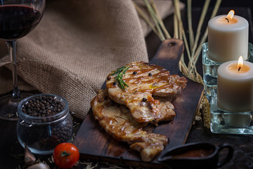 Delicious beef or pock steaks on wooden table. With the ingredients organic for cooking. Tomato and garlic. There are candles on the table. 