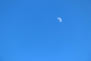 Moon lit by the sun against the blue sky