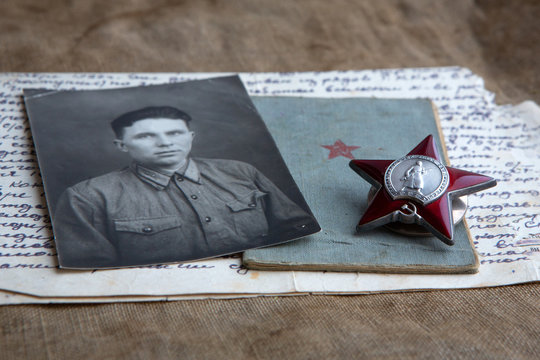 A photograph of a man in military uniform is lying next to the Order of the Red Star of the USSR and a military book. Old letter