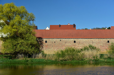 blick auf eine historische stadtmauer am fluss vor blauem himmel im frühling