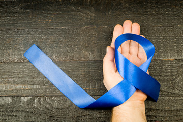 A blue ribbon on the man's hand, against the background of dark boards
