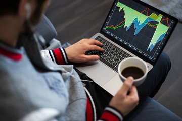 Young businessman analysing finance statistic on laptop with cup coffee in hand.