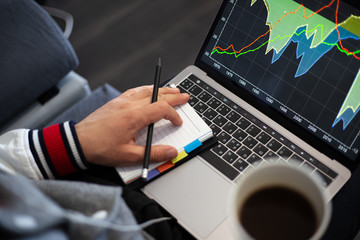 Young businessman analysing finance statistic on laptop with cup coffee in hand.