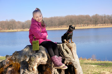 Girl sitting on a stump near the lake with a black dog PTI brabanson