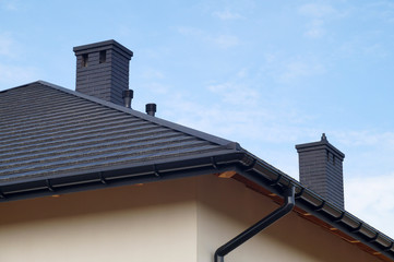 A fragment of the roof made of metal roof tiles, new chimneys. A newly built residential house.